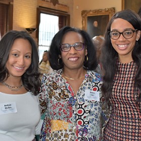 3 women smile facing camera in alumni center at reception