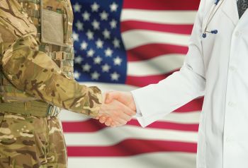 A veteran and doctor shaking hands with an American flag in the background