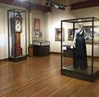 Gallery with multiple display cases one containing a dress and one a clock