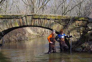 scientists stand in creek next to old bridge