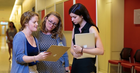 three graduate student women looking at a clipboard