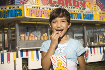 A young girl eating popcorn at a fair